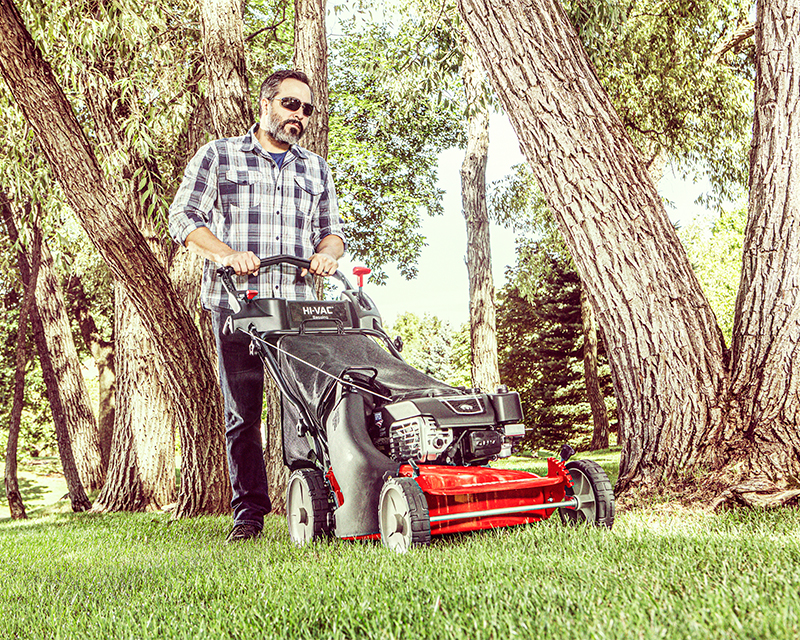 Man with sunglasses mowing his lawn with a push mower