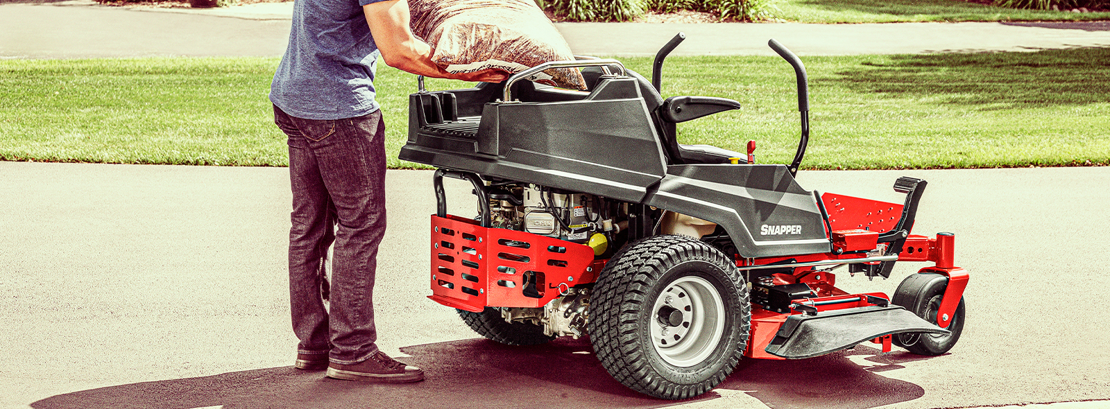 Person loading a bag of mulch on cargo bed zero turn mower attachment