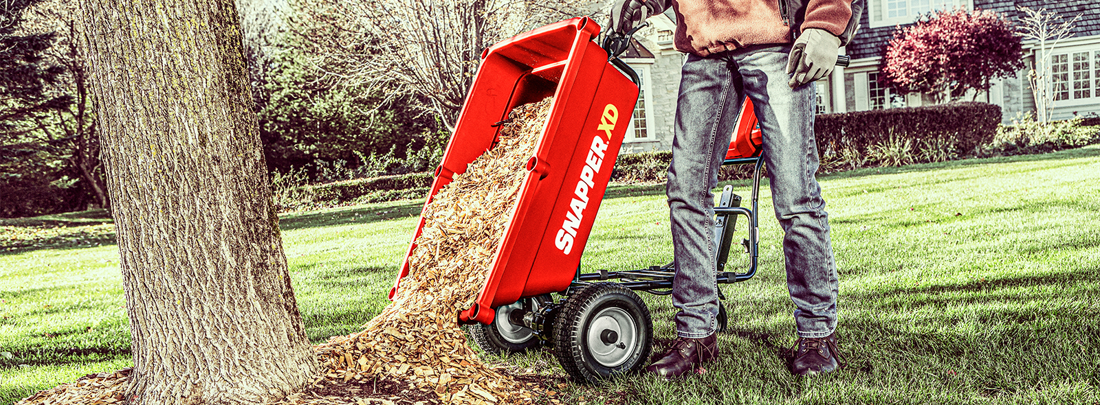 Person using Snapper utility cart to dump mulch by tree