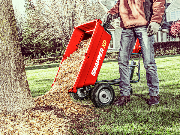 Person using Snapper utility cart to dump mulch by tree